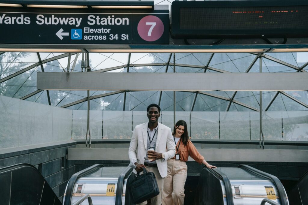 Na foto, dois profissionais alegres subindo a escada rolante de um metro no exterior. Viagens ao exterior podem ficar mais baratas em 2023 